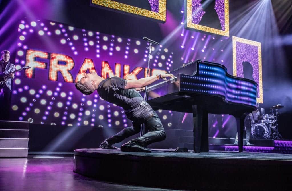 A male pianist dramatically leans backward while playing a grand piano on a stage with "FRANKIE" in lights.