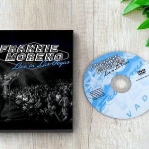 A black DVD case and a light blue DVD are on a wooden surface with green leaves. Both read "FRANKIE MORENO Live in Las Vegas."