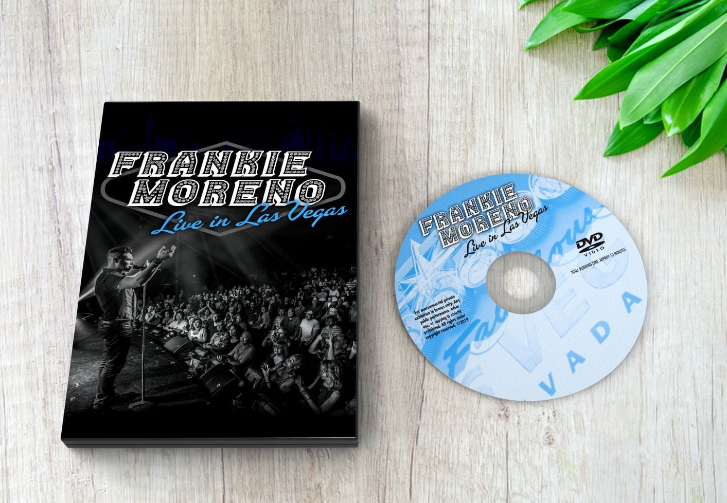 LIVE_dvd_mockup_compressed A black DVD case and a light blue DVD are on a wooden surface with green leaves. Both read "FRANKIE MORENO Live in Las Vegas."