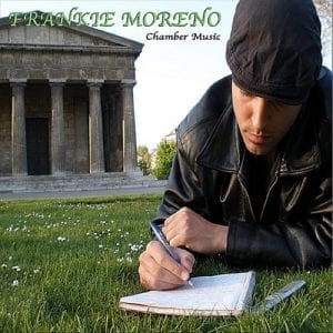 A man in a black jacket and cap writes in a notebook on grass, with "FRANKIE MORENO Chamber Music" and a stone building in the background.