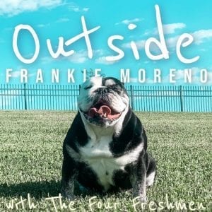 A black and white bulldog with closed eyes and tongue out sits on grass under text "Outside FRANKIE MORENO".