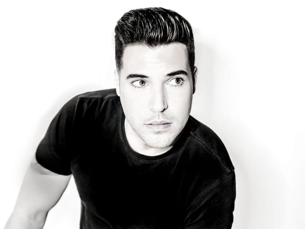 A black and white photo shows a man with dark hair and a black shirt looking to his right.