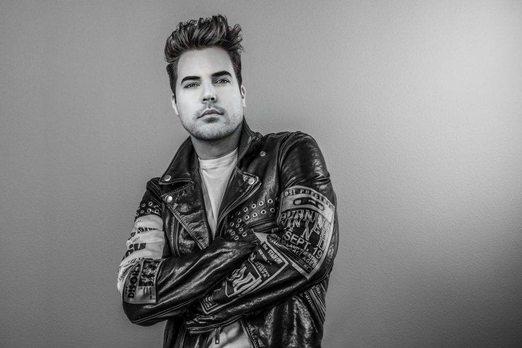 A man with styled hair and a beard wears a studded leather jacket with "SEPT. 19" on the sleeve.