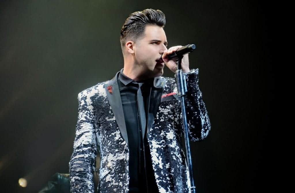 A man with slicked-back hair in a black and white sequined jacket sings into a microphone.