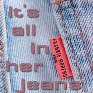 Close-up of light blue denim jeans with orange stitching and a red tag reading "FRANKIE MORENO."