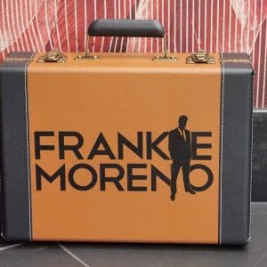 A brown and black briefcase with gold clasps and handle, featuring "FRANKIE MORENO" and a man's silhouette.
