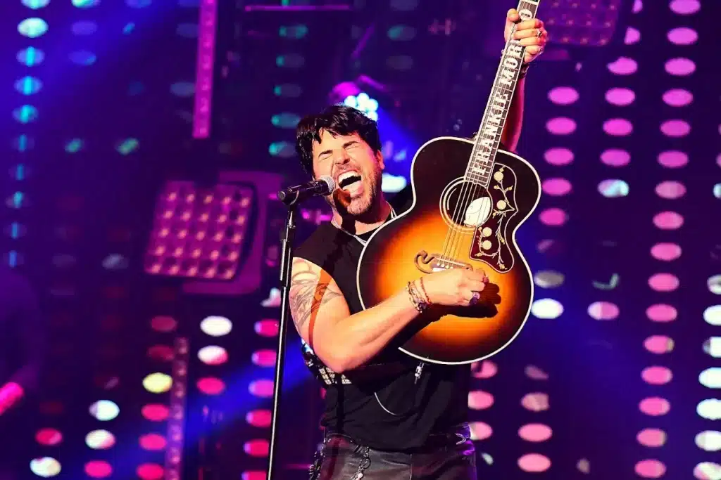 A man with dark hair sings into a microphone, holding an acoustic guitar with "TIMMY MORRISON" on the neck.