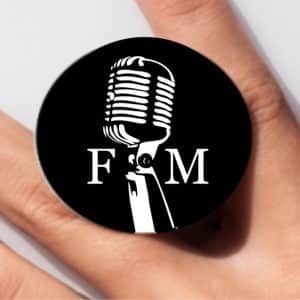 A black pop socket with a white vintage microphone and the letters "F" and "M" on a person's finger.