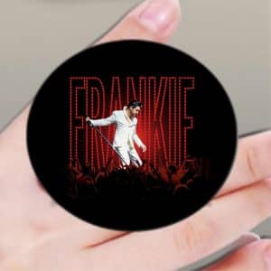 A hand holds a black pop socket with "FRANKIE" in red lights above a singer in a white suit on stage.
