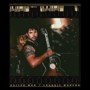 A man with dark hair and a tattooed arm holds an acoustic guitar, framed like a film strip.